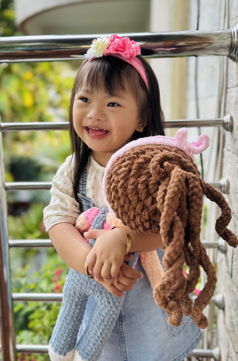 Alashi holding a knitted doll on a sunny balcony