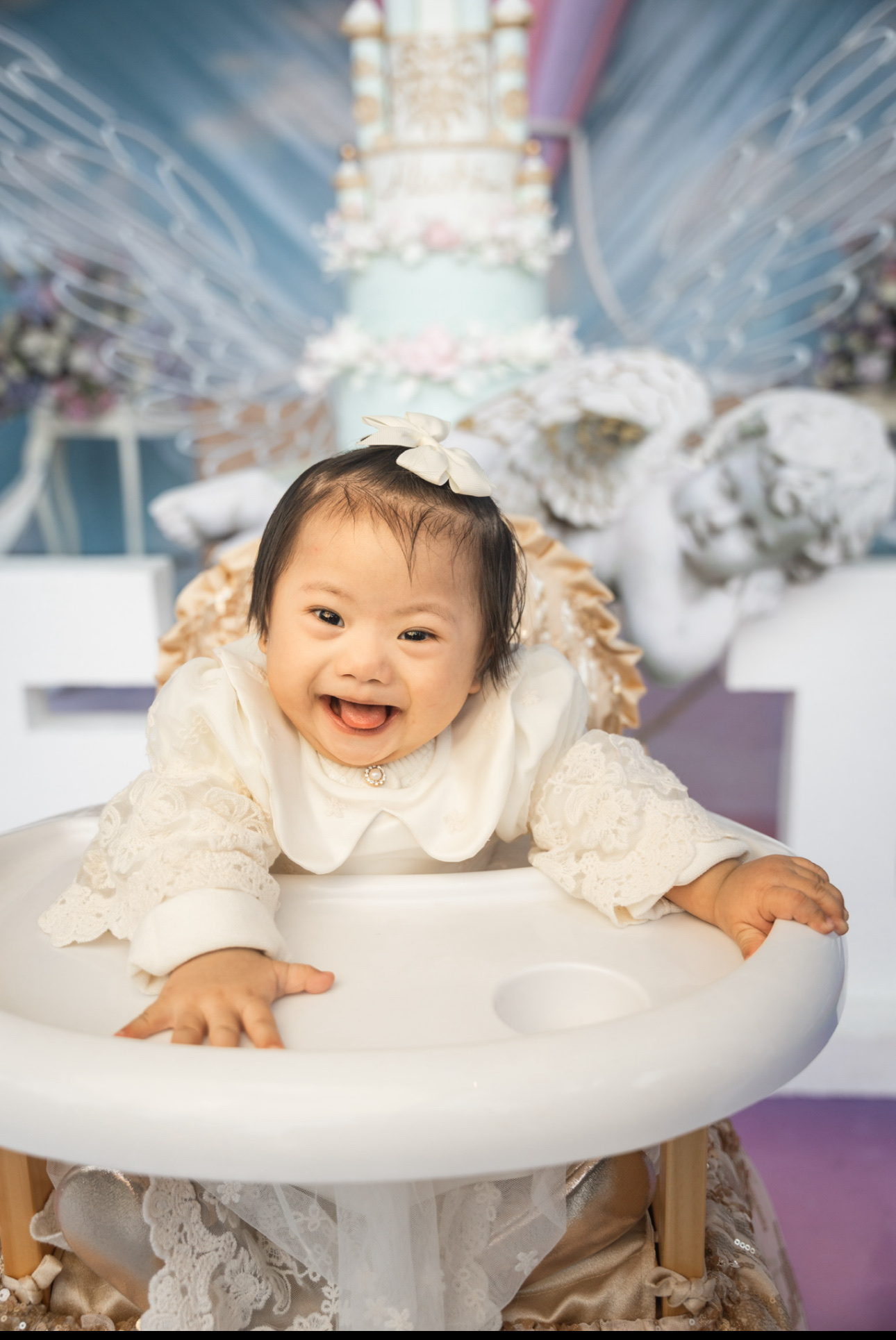Alashi as a baby, smiling in a highchair in a white dress
