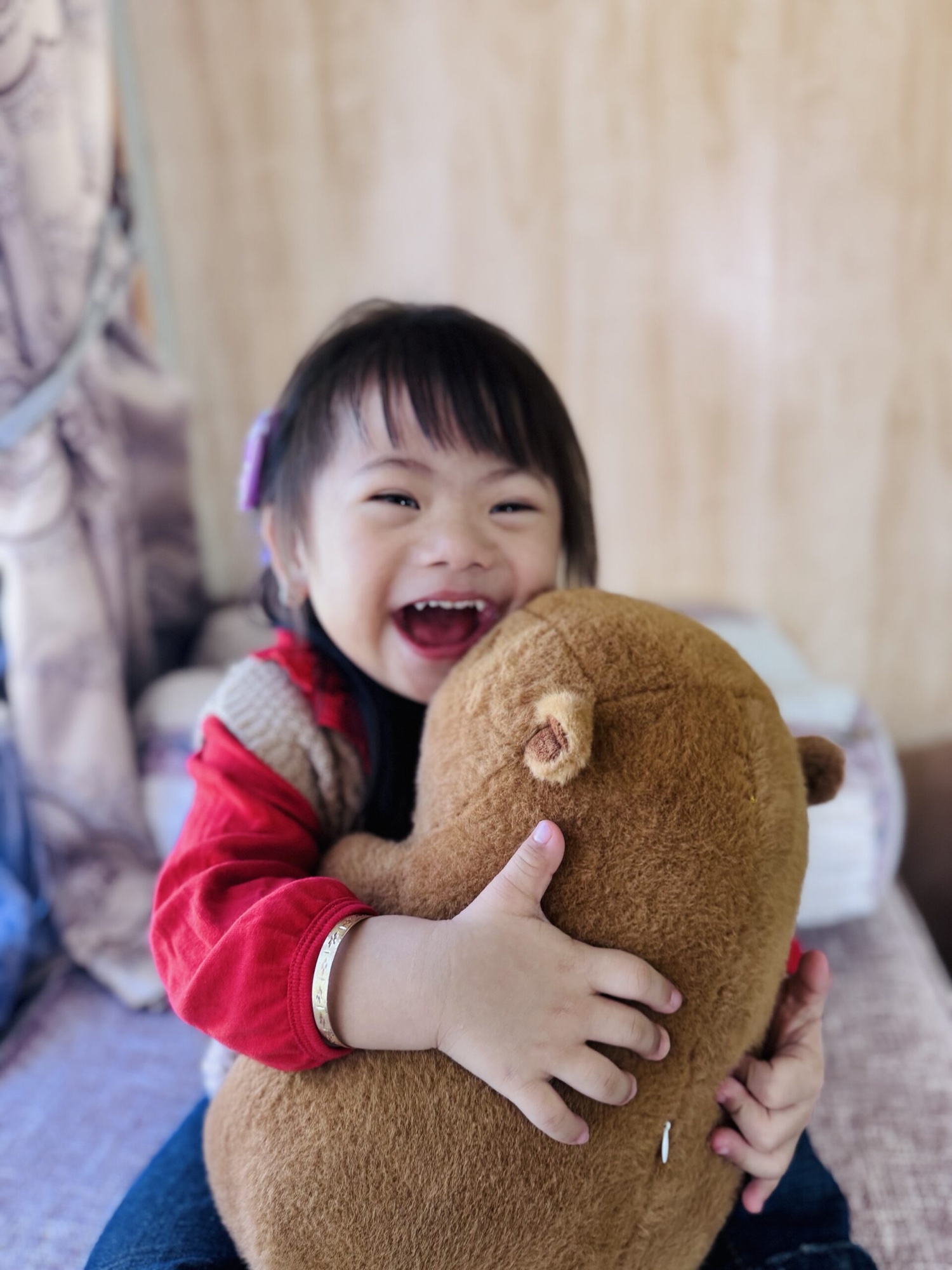 Alashi laughing and hugging a large brown teddy bear