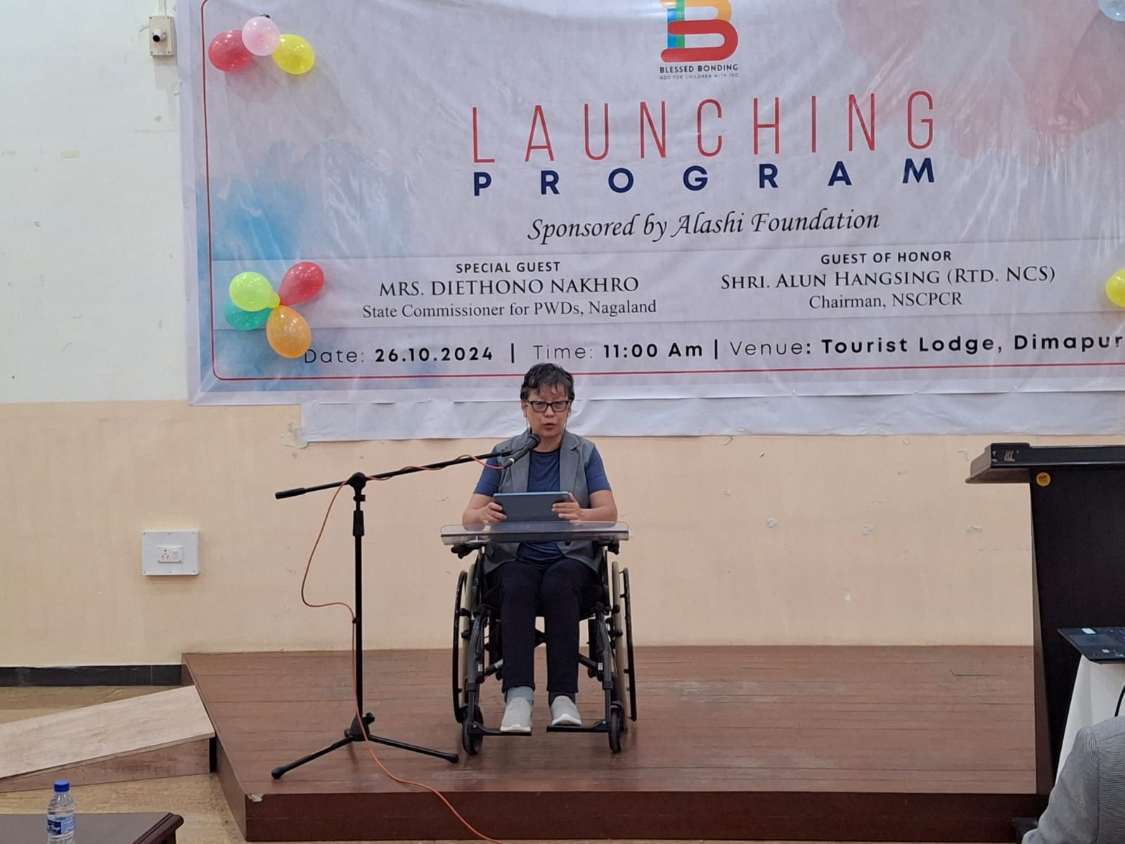 A speaker in a wheelchair addresses the audience at the Alashi Foundation launch programme